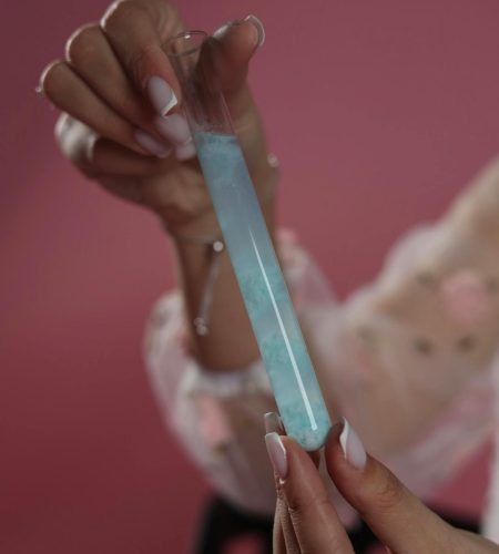 Close-up of a woman holding a test tube with blue liquid against a pink wall, highlighting the concept of science.