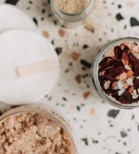 Flat lay of natural bath essentials including scrub and cotton pads on a terrazzo surface.